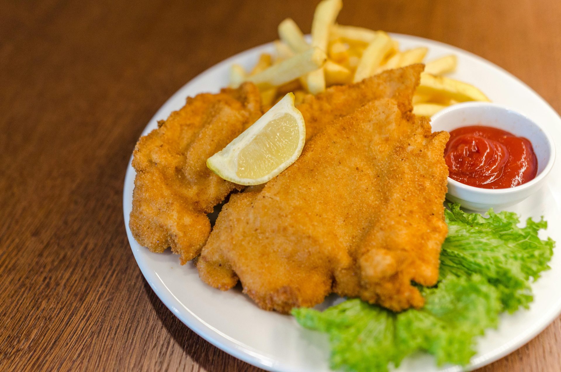 Köstliches Schnitzel, serviert mit Pommes frites, Salat, Zitrone und Ketchup auf einem Holztisch.